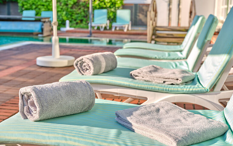 Liebevoll vorbereitete Sonnenliegen mit einem Pool und Sonnenschirm im Hintergrund.